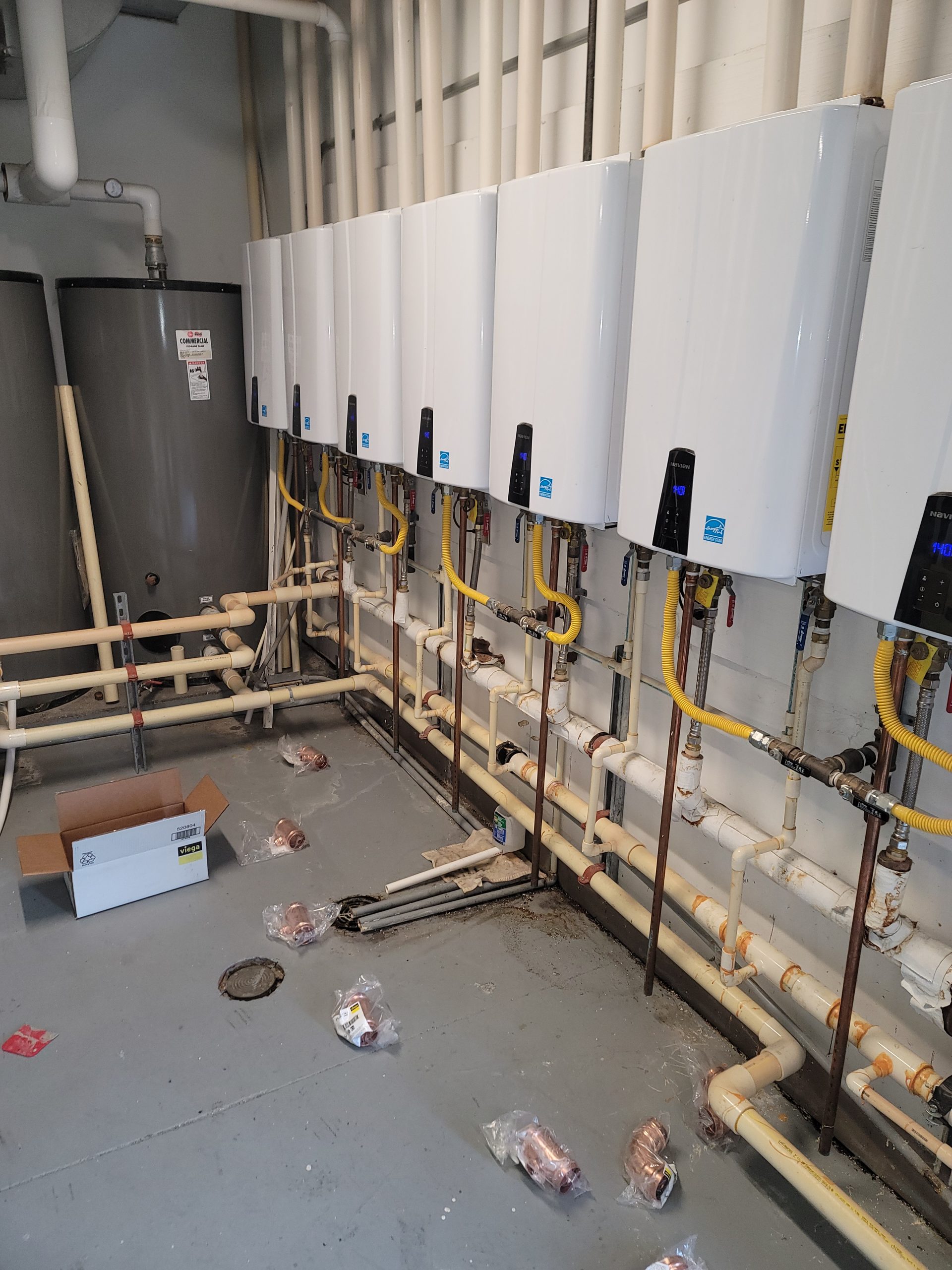 Multi-unit commercial tankless water heater installation showing eight Navien units in series with backup commercial storage tank