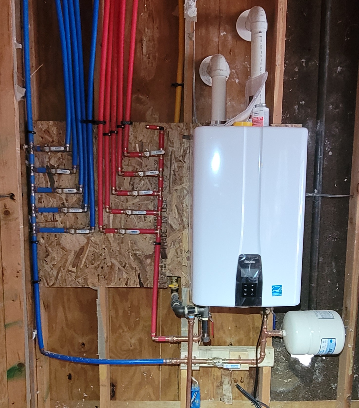 Recent residential new-construction Navien tankless water heater installation by Critical Plumbing — clean PEX manifold, copper supply, expansion tank, code-compliant venting